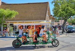 Children waving from a long green surrey cycle with a yellow canopy on a Solvang street