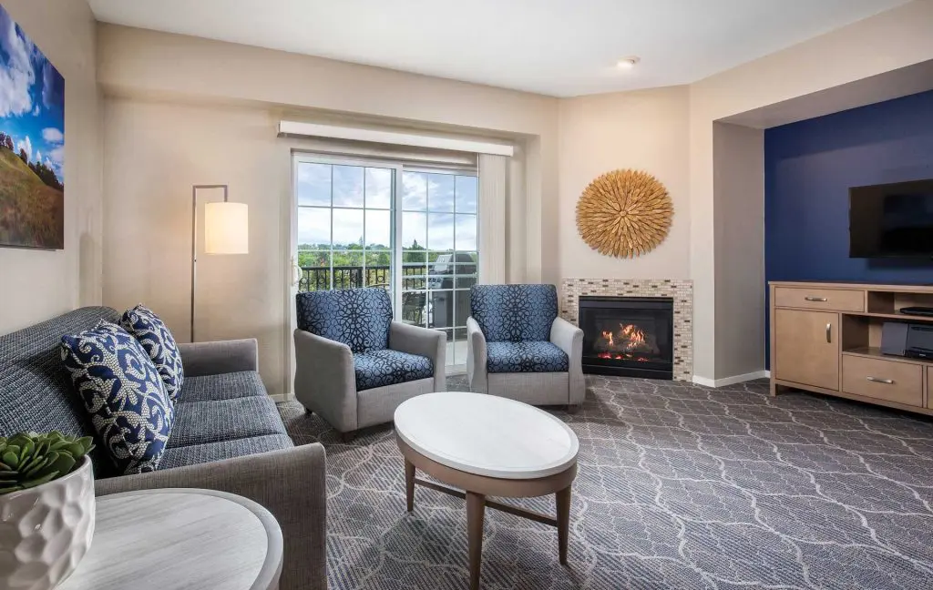 A WorldMark Solvang living room with a lit fireplace, patterned armchairs and a balcony door